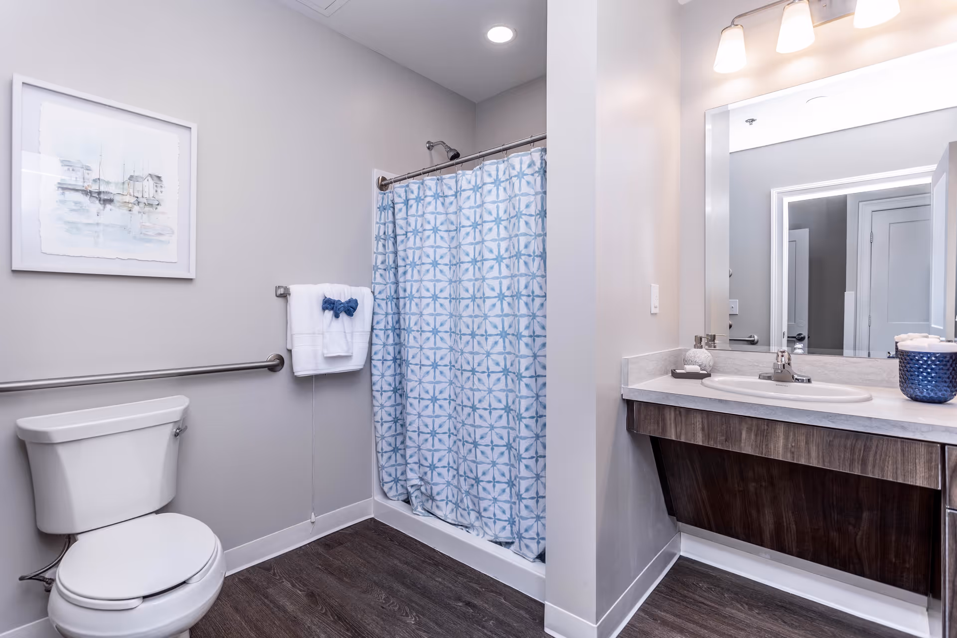 Accessible bathroom featuring a toilet with grab bar, a shower with a blue patterned curtain, and a vanity sink with mirror.