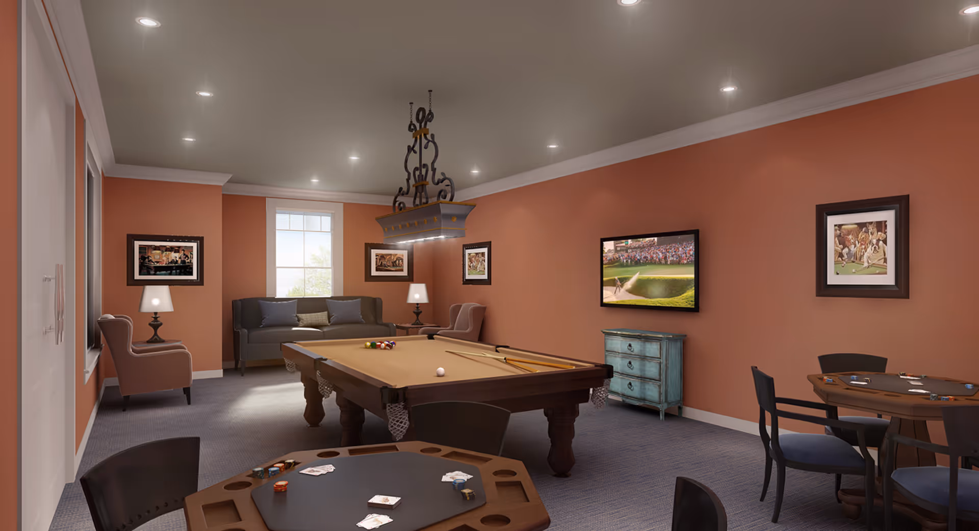 A recreational room with a pool table in the center, two card tables with chairs, a gray sofa and armchairs near a window, framed pictures on the walls, a flat-screen TV mounted on the wall, and a decorative light fixture hanging above the pool table.