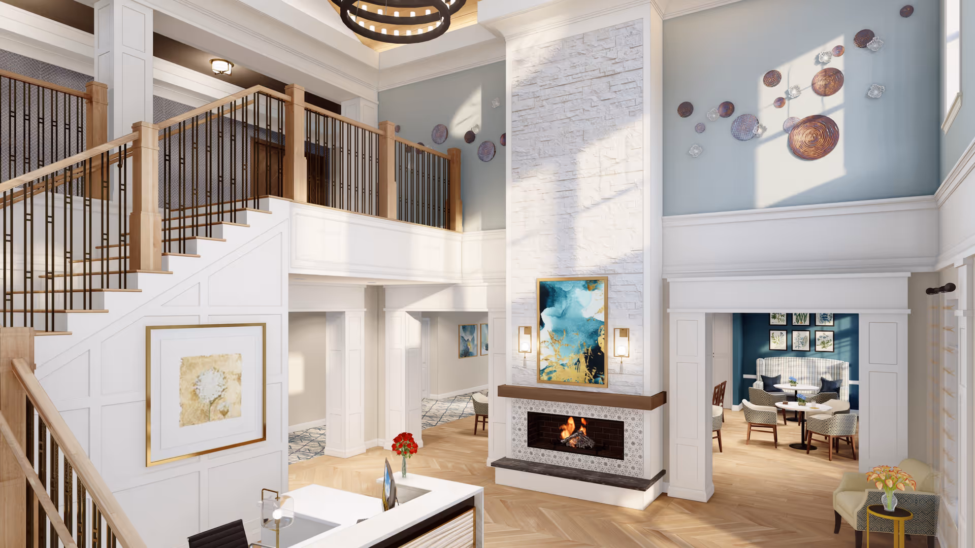 A bright and spacious senior living facility interior featuring a two-story area with a staircase and railing, a modern fireplace with artwork above it, and a seating area with chairs and tables visible through an open doorway. The space is decorated with wall art, a chandelier, and natural light streaming in through windows.