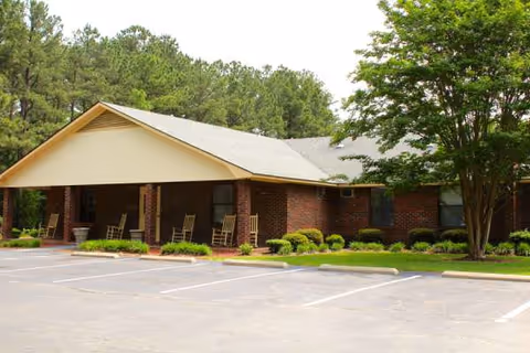 Single-story brick assisted living facility exterior with a covered entrance and rocking chairs.