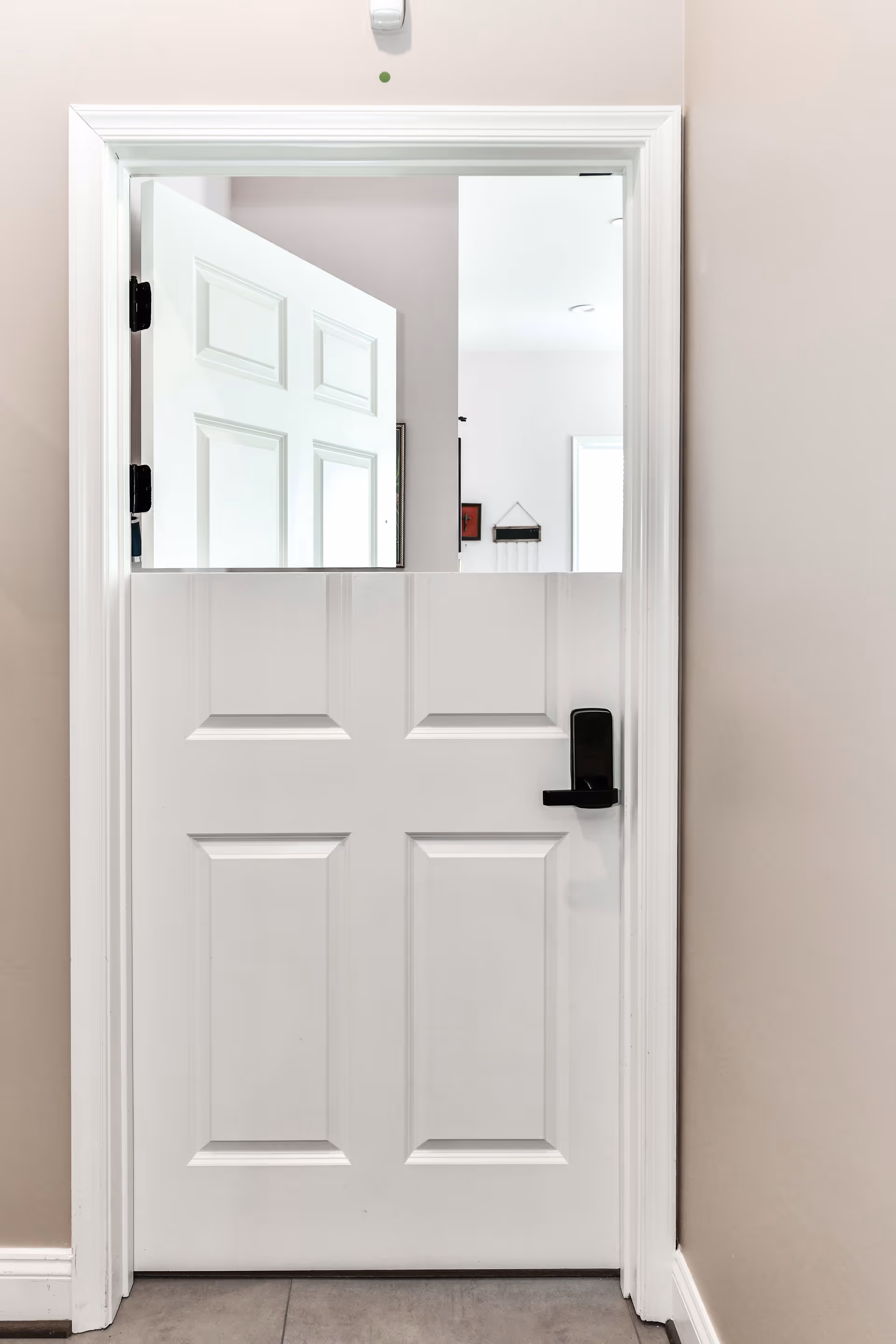 White interior Dutch-style door with the top half open, black lever handle, and a mirror reflecting an adjacent room.