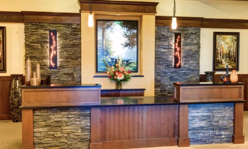 Reception desk area with stone and wood paneling, two pendant lights, decorative vases, and framed nature artwork on the walls behind the desk.
