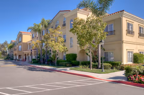 Exterior view of a multi-story beige senior living building with palm trees and landscaped grounds.