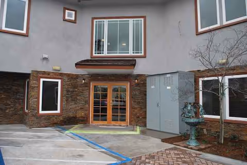Exterior view of Ramona Senior Manor entrance with double wooden doors and brick and stone facade.