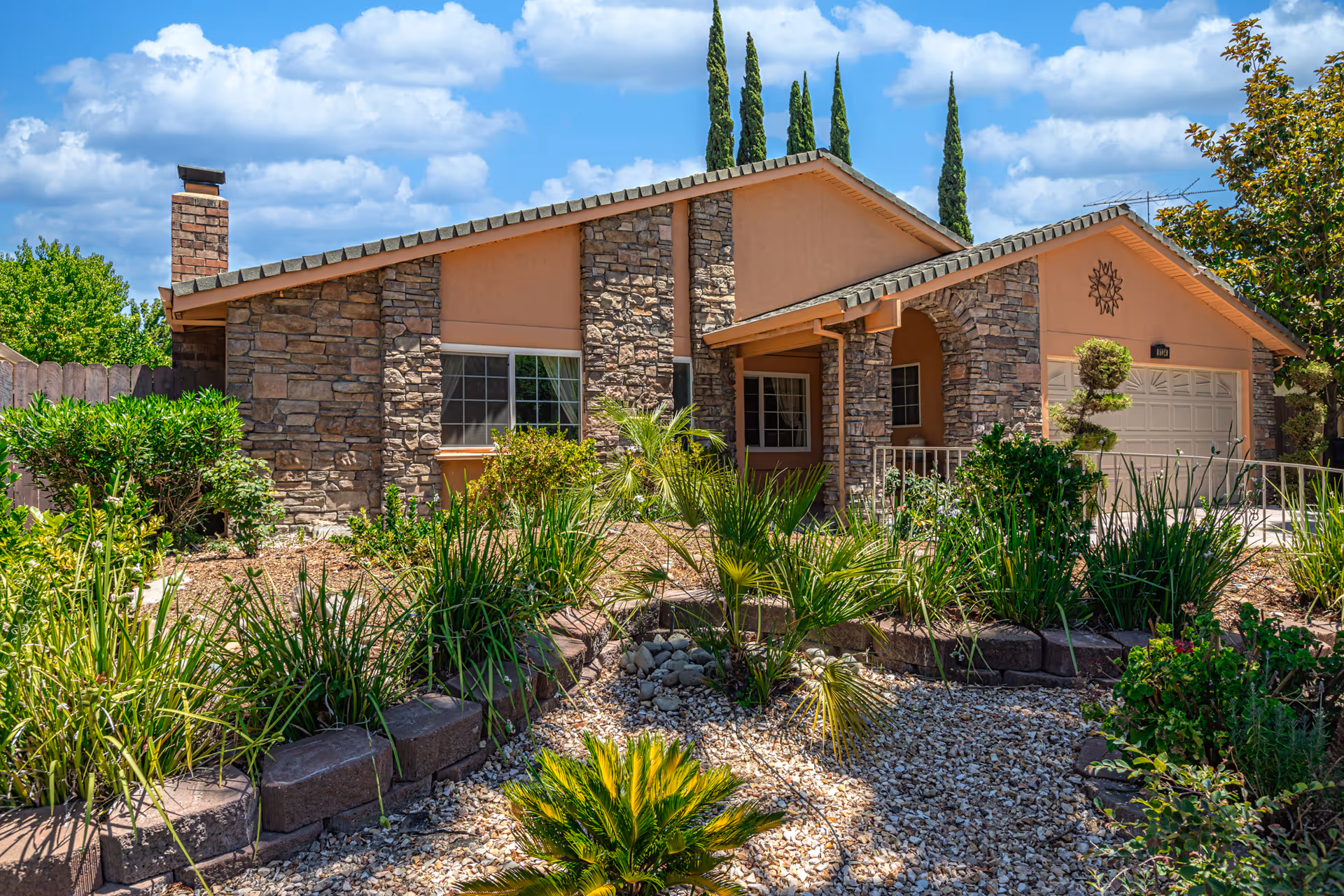 Single-story stone and stucco house with a landscaped front yard and attached garage under a blue sky.