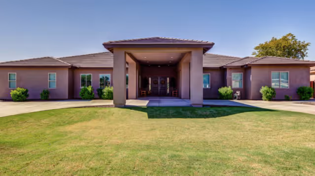Front exterior view of Quail Manor Assisted Living building with a covered entrance, brown walls, multiple windows, and a well-maintained green lawn in front.