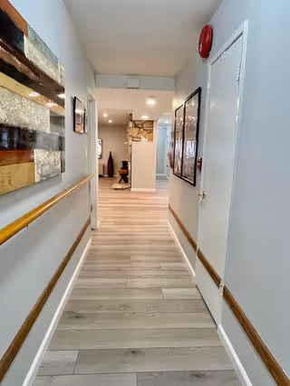 Well-lit interior hallway with wood handrails and light wood flooring leading to a sitting area with a stone fireplace.