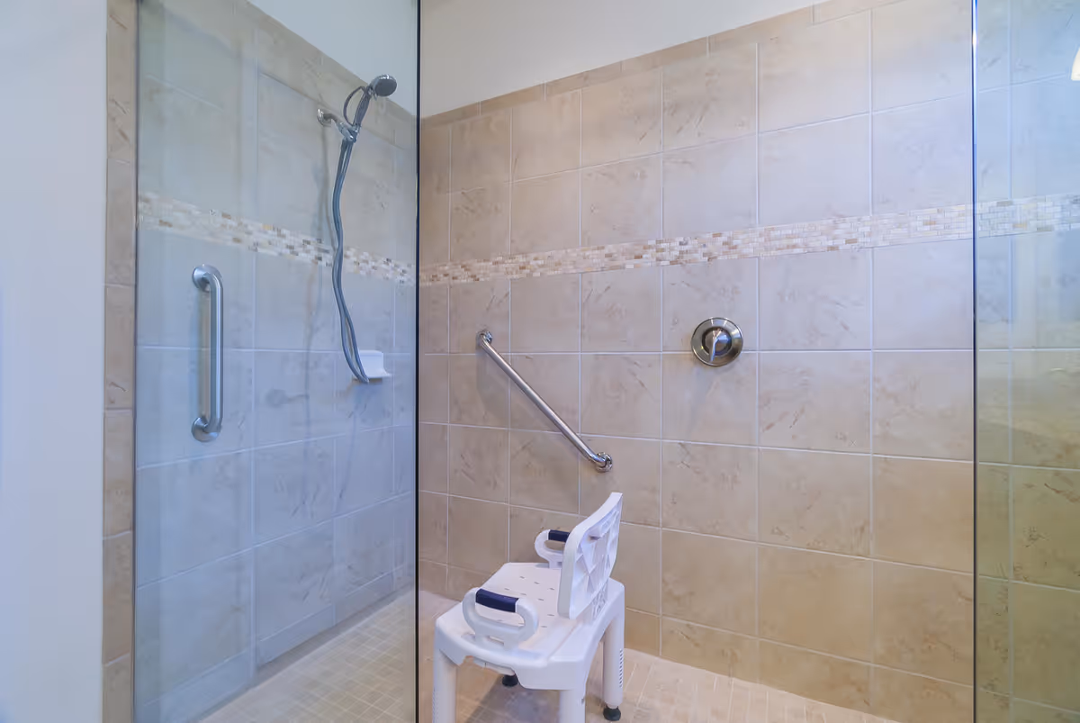 Tiled accessible walk-in shower with grab bars, a handheld showerhead, and a white shower chair.