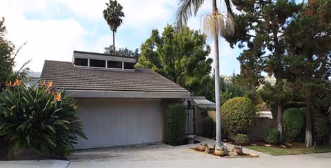 Front exterior of Orange County Care Home with garage doors, driveway, and palm trees.