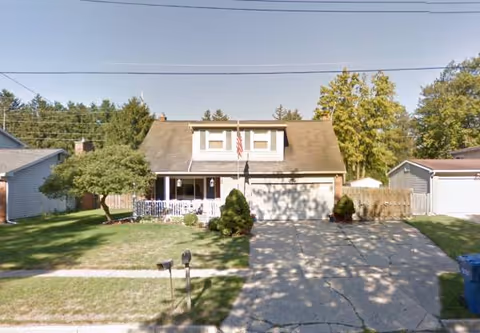 Front view of a suburban home with a driveway, lawn, and American flag.