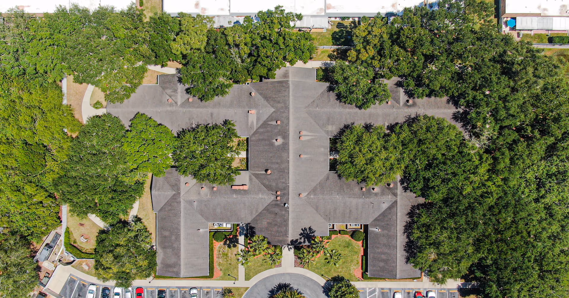 Aerial view of Arden Courts - ProMedica Memory Care Community (Largo) showing the building's roof surrounded by trees, parking spaces with cars, and landscaped green areas.