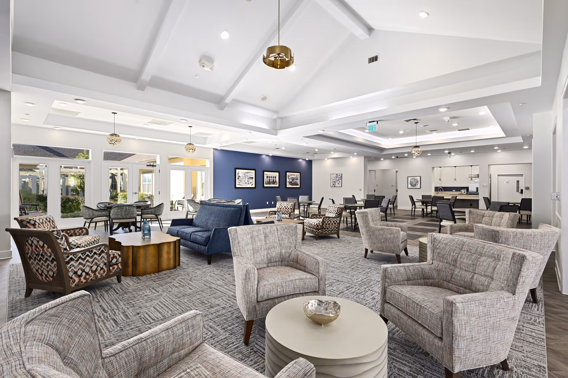 Bright, modern communal lounge with multiple seating areas, tables, and a kitchenette in the background.