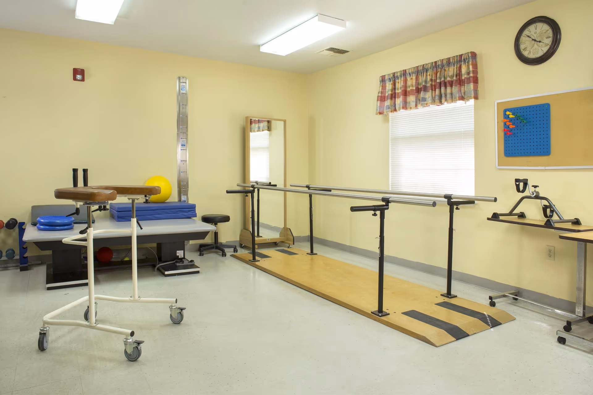 Rehabilitation therapy room with parallel bars, treatment table, exercise balls, and mobility equipment.