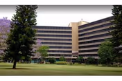 Large multi-story curved building with rows of balconies facing a grassy lawn and trees.