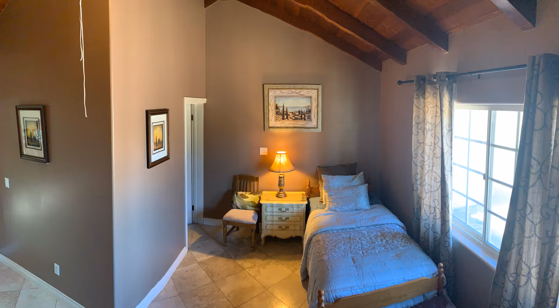 Cozy bedroom in a senior facility with a single bed, nightstand, lamp, and window.