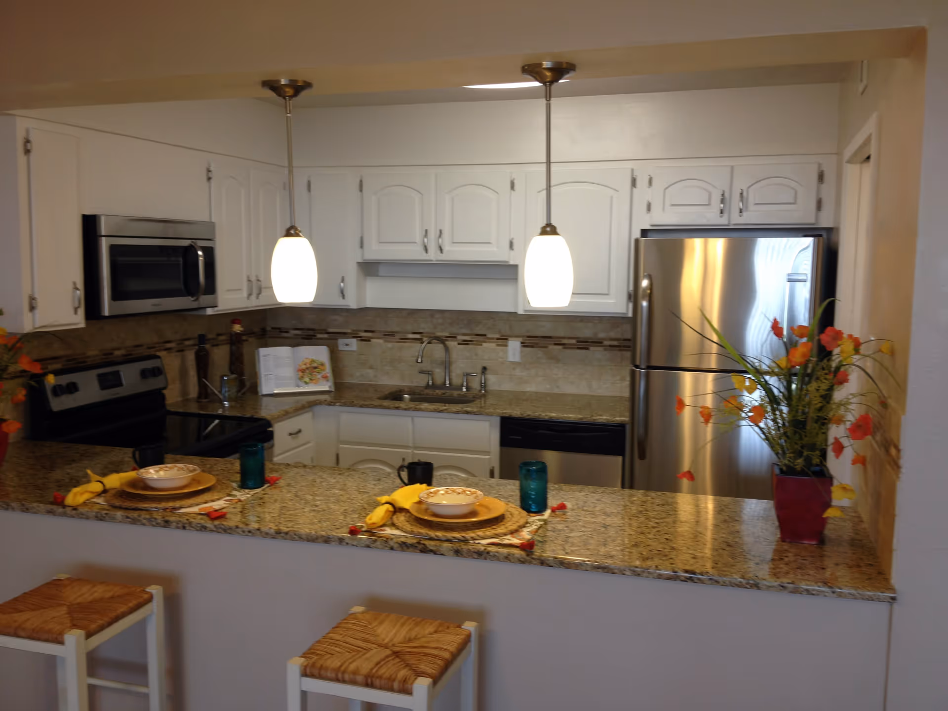 Bright kitchen with a granite countertop breakfast bar, white cabinets, stainless steel appliances, two pendant lights and two stools.