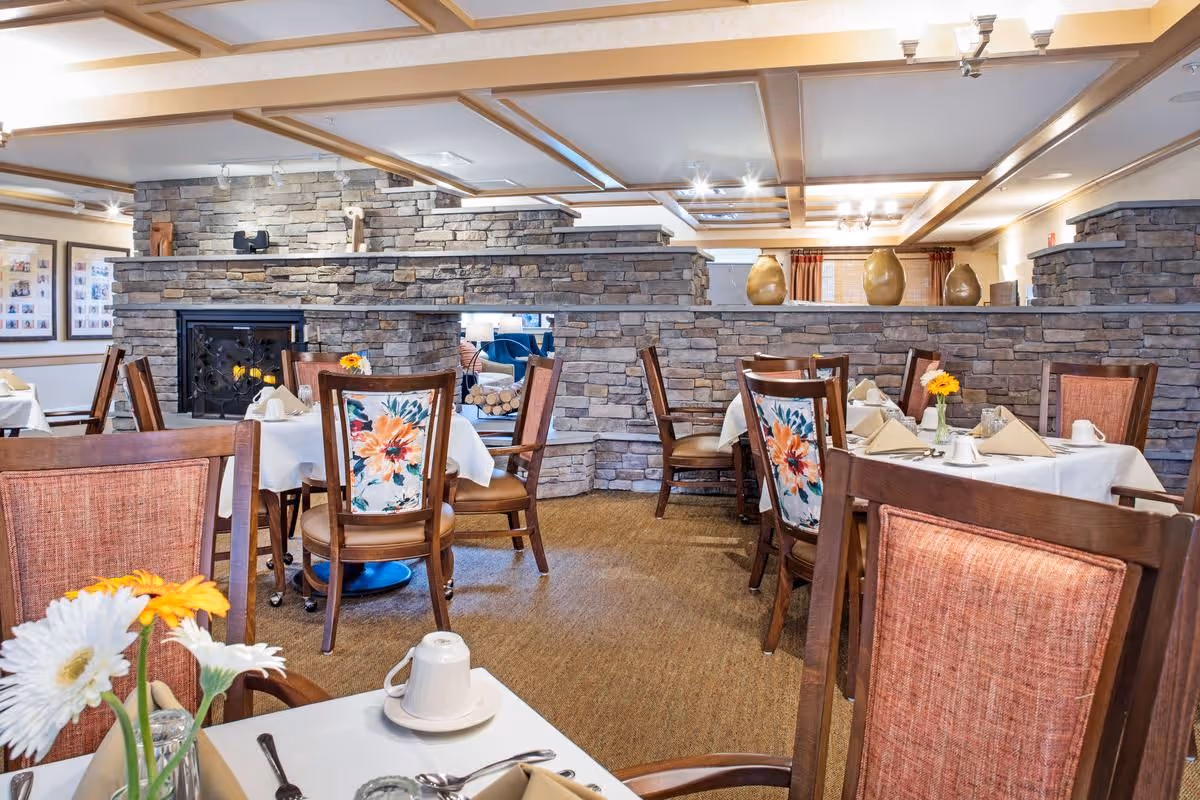 Dining room with tables set for meals, floral-upholstered chairs, and a stone partition topped with decorative vases.
