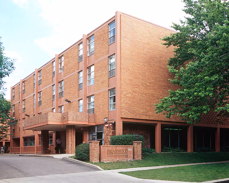 Four-story brick building with a covered entrance and a sign reading 'Briarwood' on the lawn.