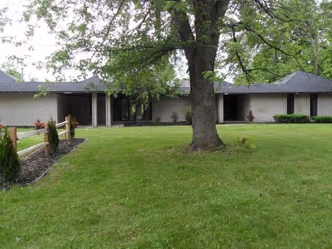 Single-story brick building front with a large tree and a grassy lawn.