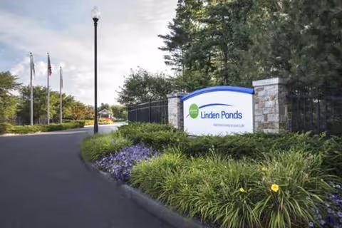 Entrance to Linden Ponds with stone pillars, a sign, and landscaped greenery.