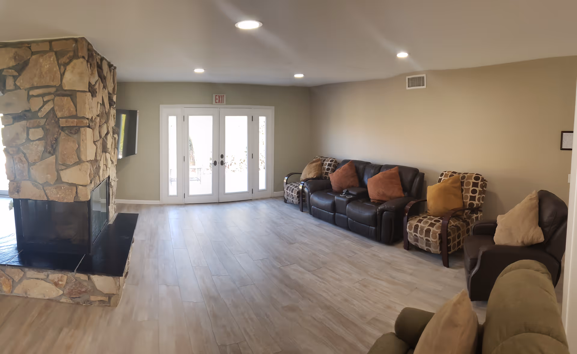 A cozy living room area with a stone fireplace, multiple couches, and large glass doors leading outside.