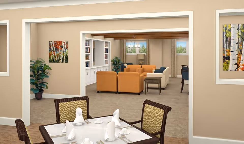 View of a senior living facility interior showing a dining area with a table set with white napkins and cups in the foreground, and a living room with orange and white sofas, a side table, plants, and artwork on the walls in the background.