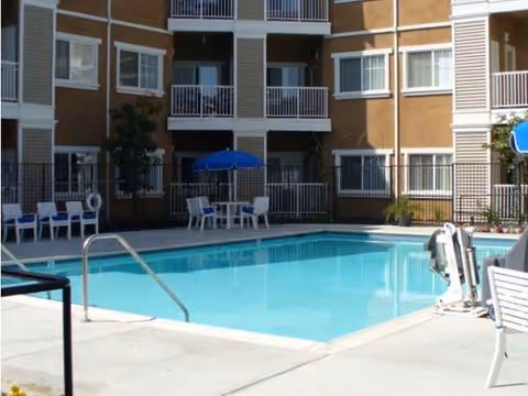Outdoor swimming pool at a senior living complex with lounge chairs and umbrellas.
