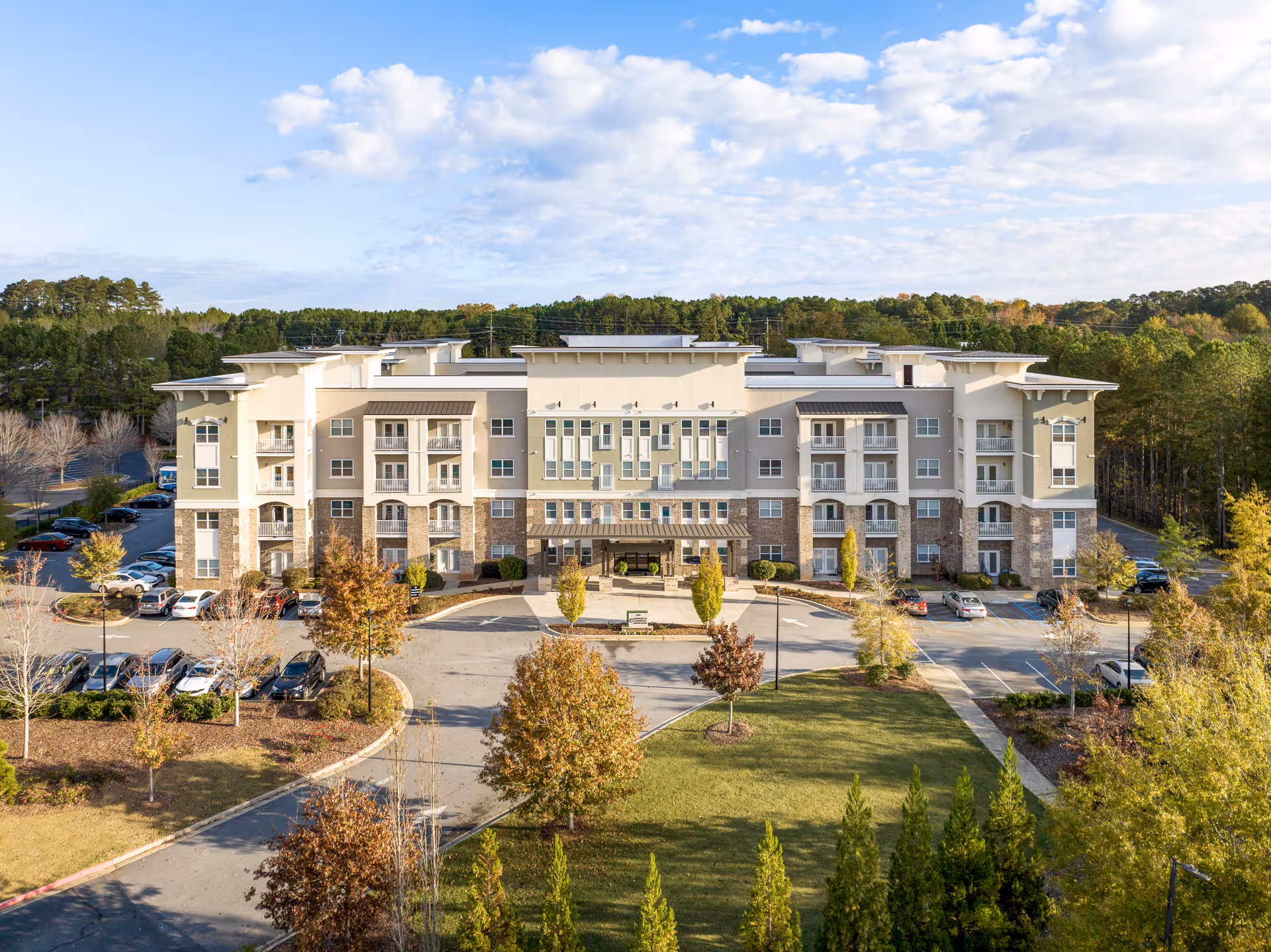 Front exterior of a four-story residential building with a porte-cochère, parking lot, and landscaped grounds.