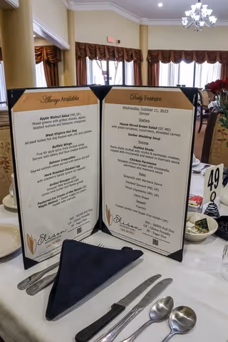 A dining table set with a menu featuring daily specials and always available items at Elison Independent Living of Lake Worth, with utensils and a napkin neatly arranged.