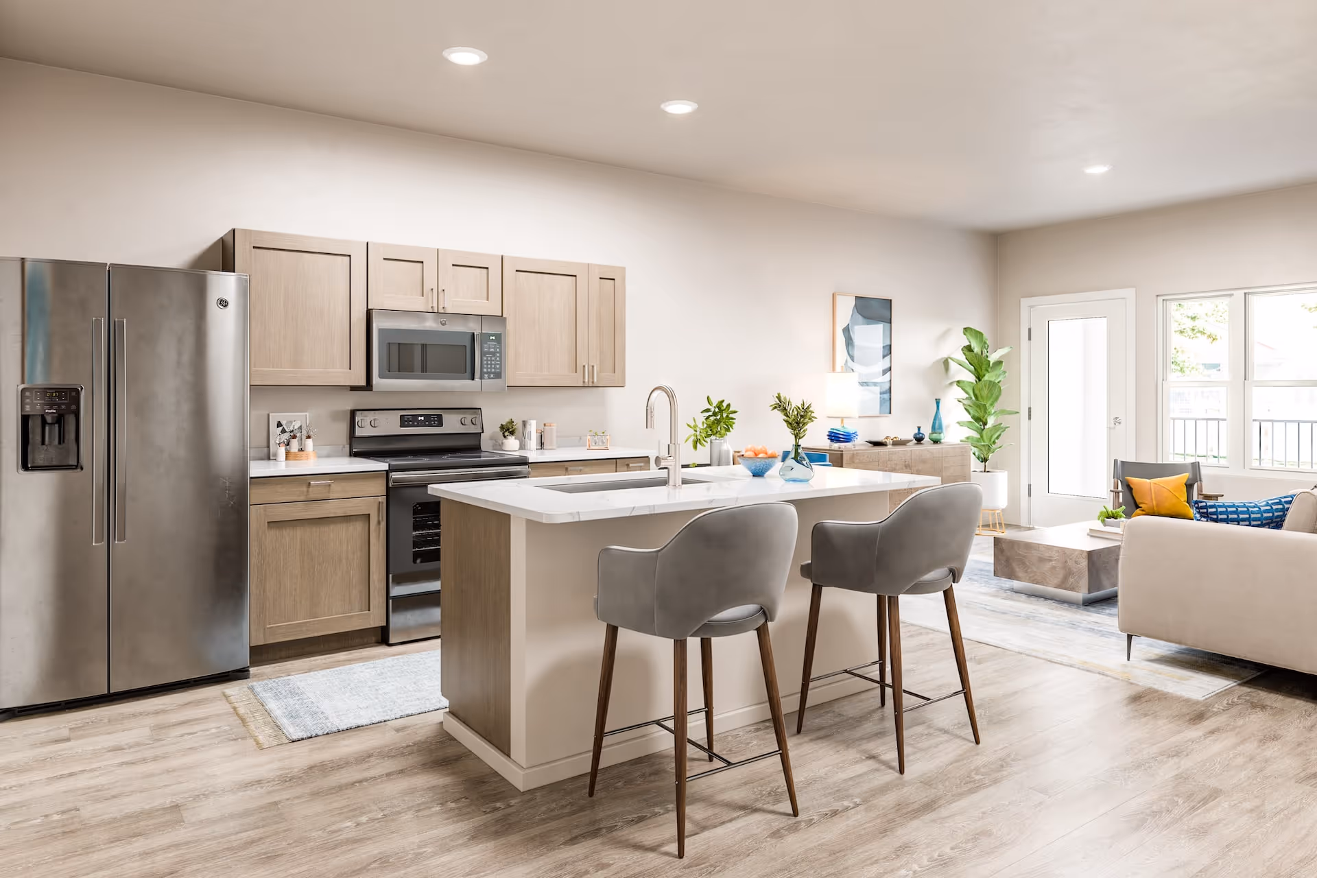 Bright open-concept kitchen with a central island, two barstools, stainless steel appliances, and a connected living area.