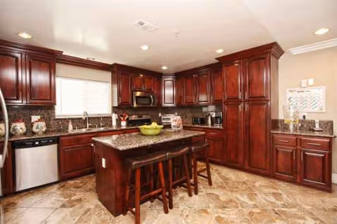 A spacious kitchen with dark wood cabinets, granite countertops, and a central island with stools.