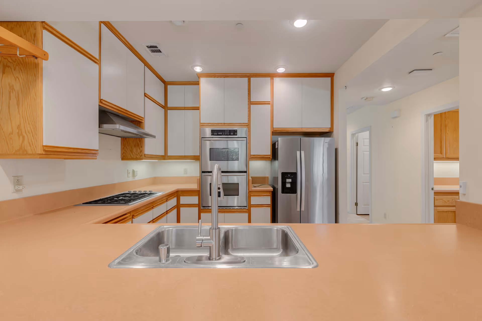 Bright kitchen with a center island sink, stainless steel appliances, and wood-trimmed white cabinets.