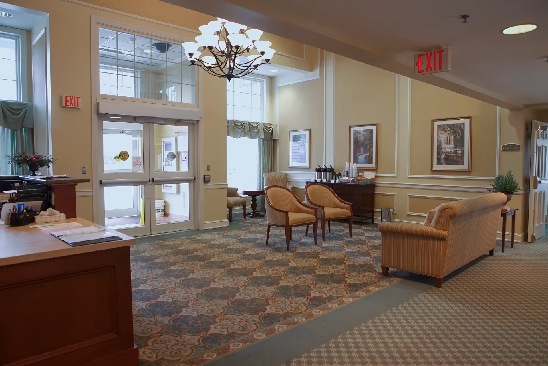 A senior living facility lobby with seating, a chandelier, and double glass entrance doors.
