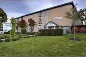 Front view of a beige two-story senior living facility with entrance canopy and landscaped lawn.