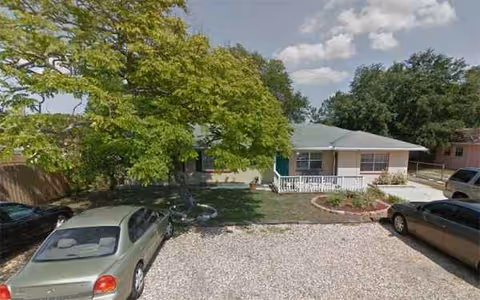 A single-story residence with a front porch, gravel driveway, and parked cars.