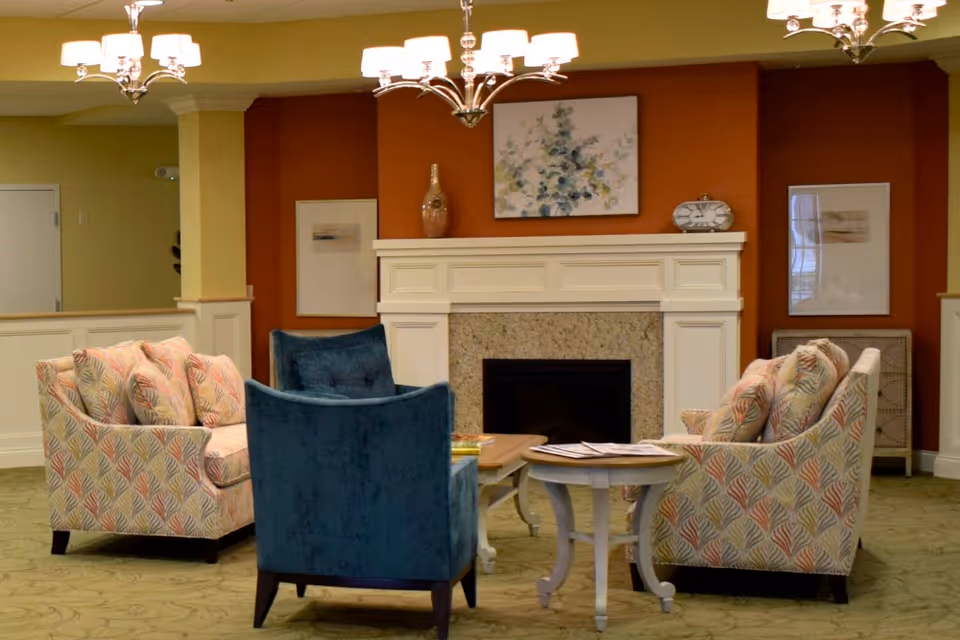 Cozy lounge area with upholstered chairs and a small table arranged around a fireplace and mantel.