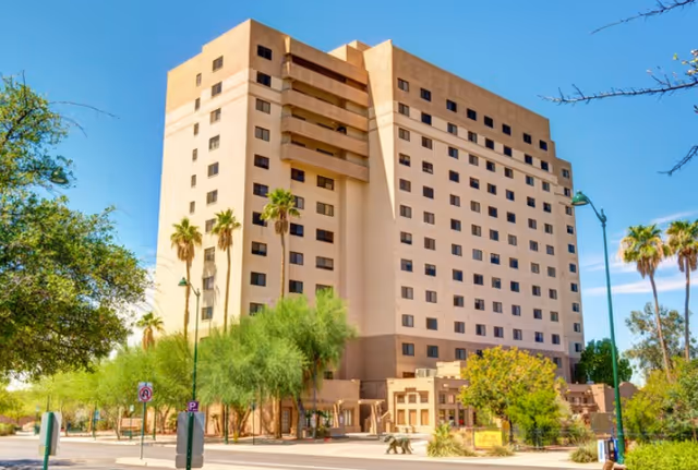 Exterior view of a tall beige senior living building with palm trees.
