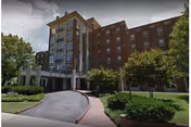 Multi-story brick building exterior with a covered drive-up entrance, circular driveway, and landscaped grounds.