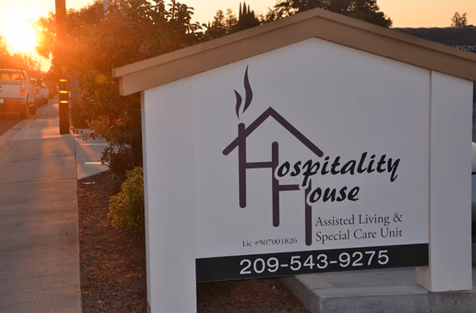 Outdoor sign for Hospitality House Assisted Living & Special Care Unit with phone number along a sidewalk at sunset.