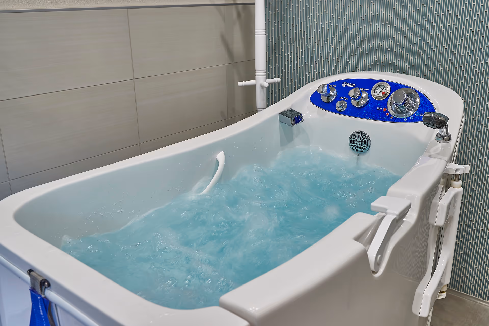 A hydromassage bathtub filled with bubbling blue water and a control panel against tiled walls.