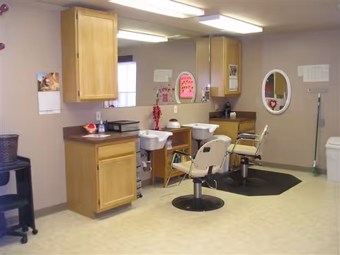 Salon area with two styling chairs and washbasins, mirrors, and wooden cabinets in a retirement community room.