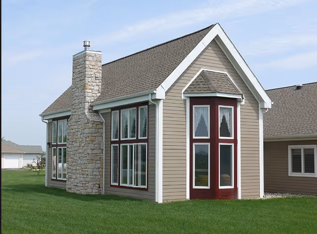 Exterior view of a small house-like building with large windows, a stone chimney, and a green lawn.