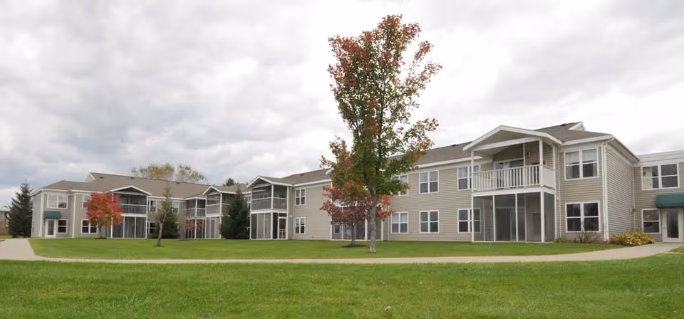 Exterior view of Prestwick Chase at Saratoga with lawn, trees, and apartment buildings.