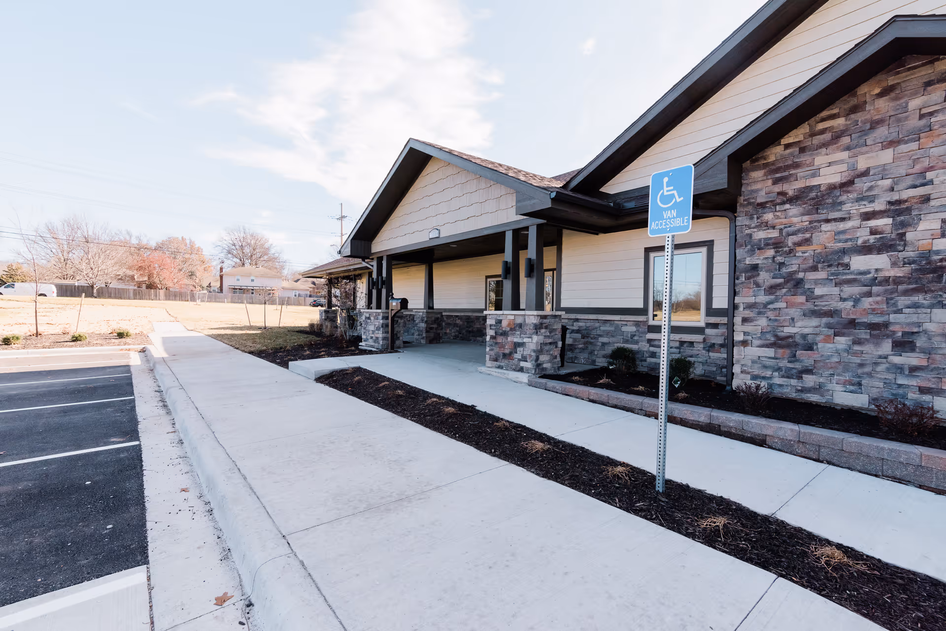 Front entrance of a single-story building with stone siding, a sidewalk, and a van-accessible parking sign.