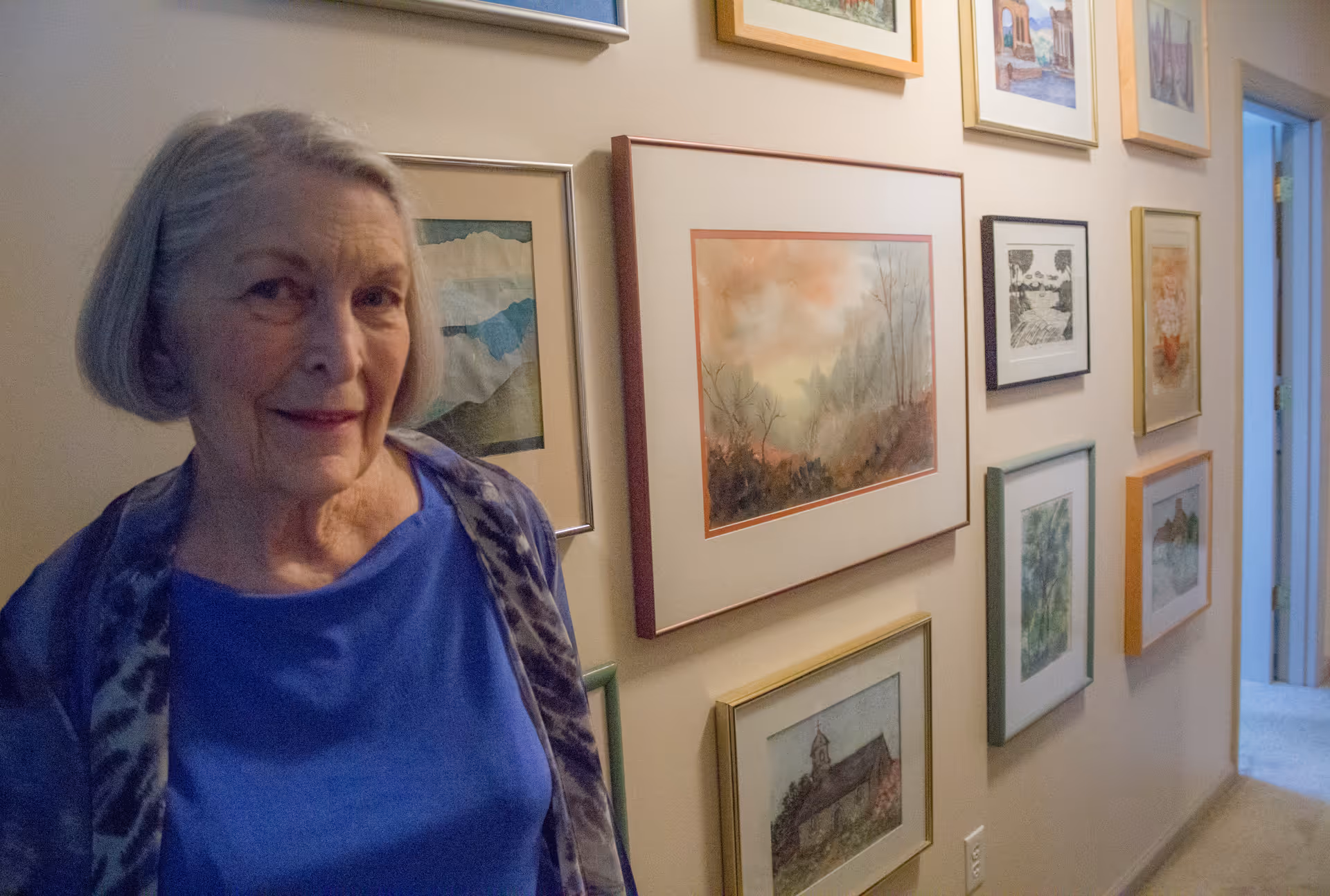 A woman standing in a hallway lined with framed paintings and prints.
