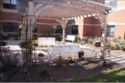 Outdoor courtyard at Southington Care Center with a white pergola, benches, and planters.
