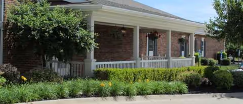 Windmill Manor exterior: brick building with shaded front porch, columns, and landscaped entry.