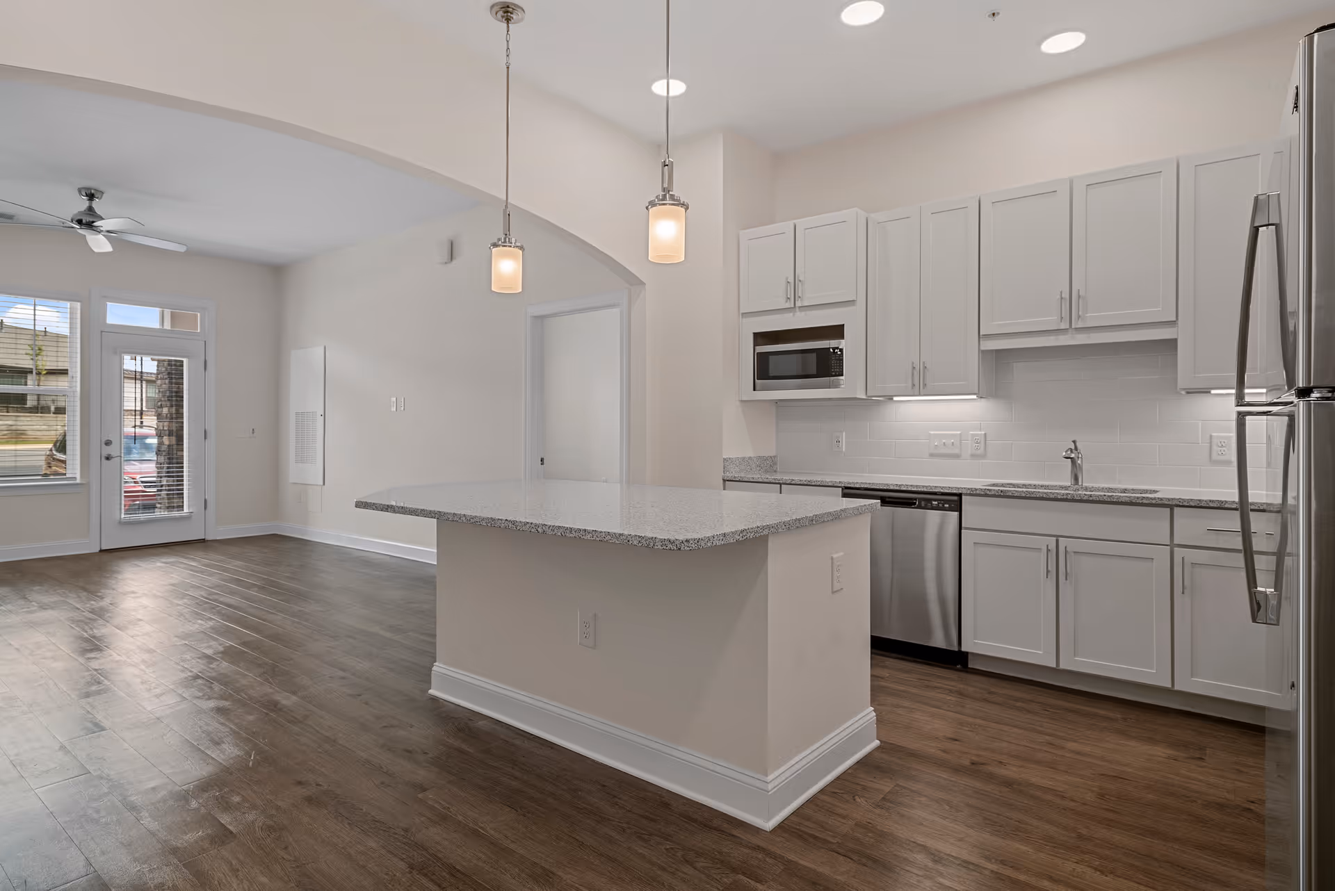 Open-plan kitchen with a central island, white cabinets, stainless-steel appliances, and hardwood floors opening to a living area.