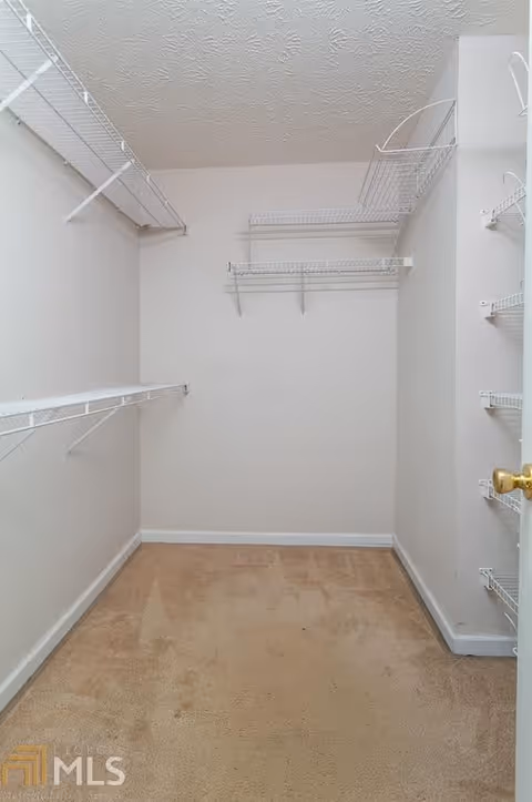 Empty walk-in closet with beige carpet and white wire shelving on three walls under a textured white ceiling.