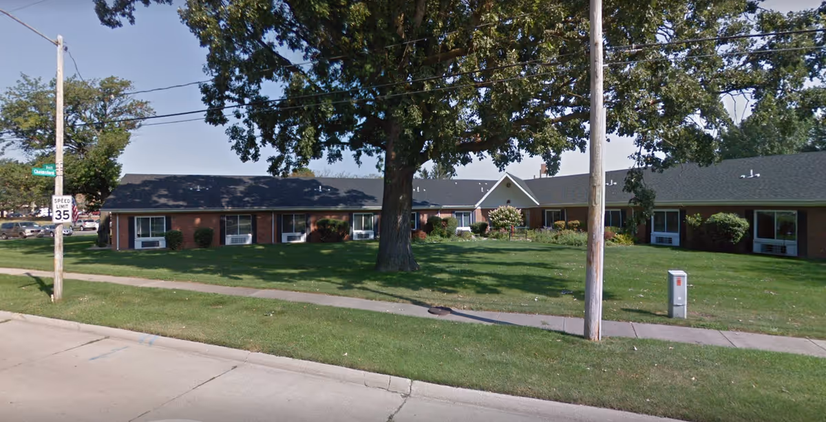 Exterior view of a single-story brick senior living facility with lawn and trees.